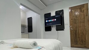 A hotel room with a bed, a television mounted on the wall, a wooden door, and a bathroom visible in the background. - We provide transport going to shopping center, restaurants and tourism office. (Donsol)