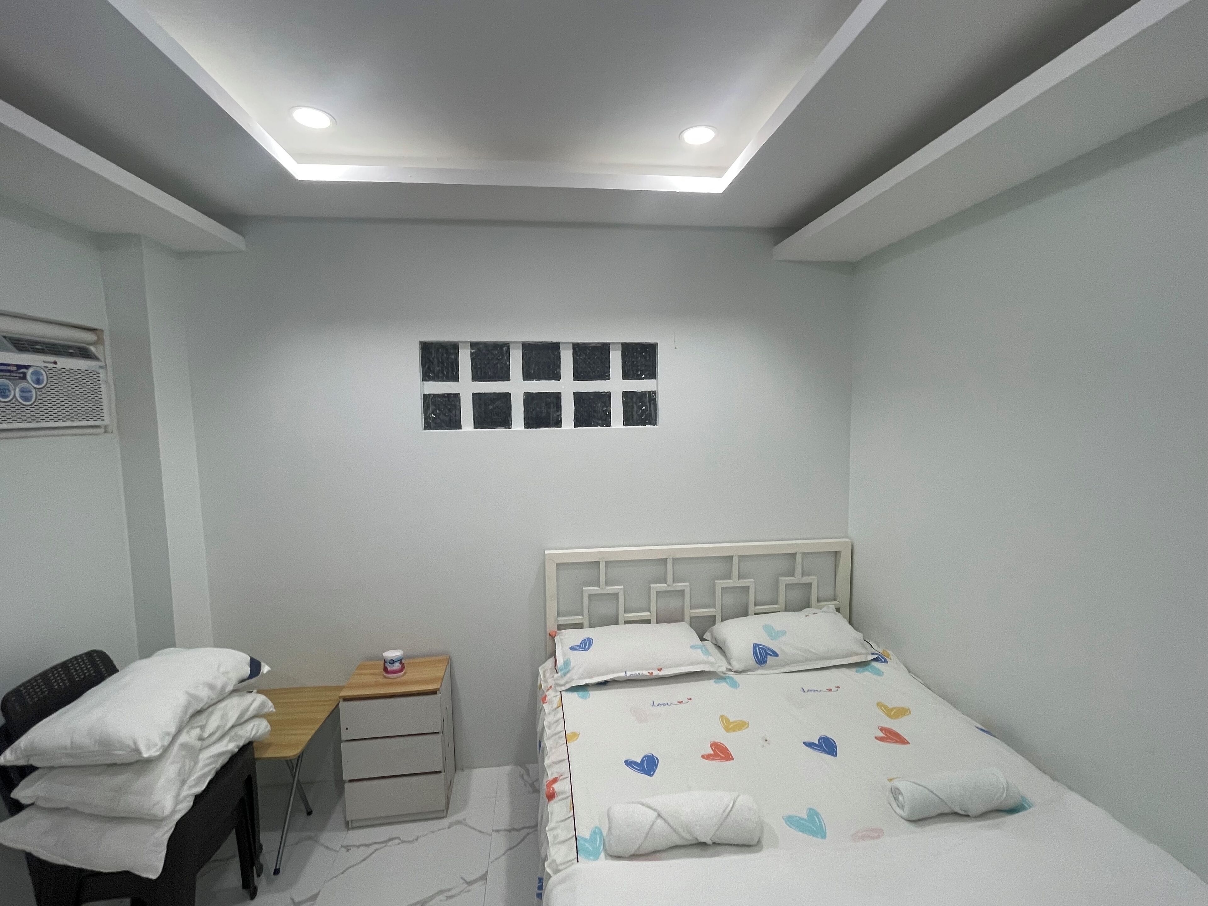 A bedroom with a bed, a desk, and a chair. There is a window with blinds on the wall.