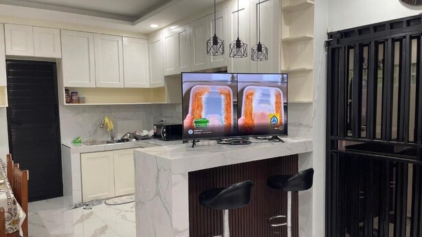 A modern kitchen with white cabinets, a marble countertop, a built-in TV, and two black bar stools. - We provide transport going to shopping center, restaurants and tourism office. (Donsol)