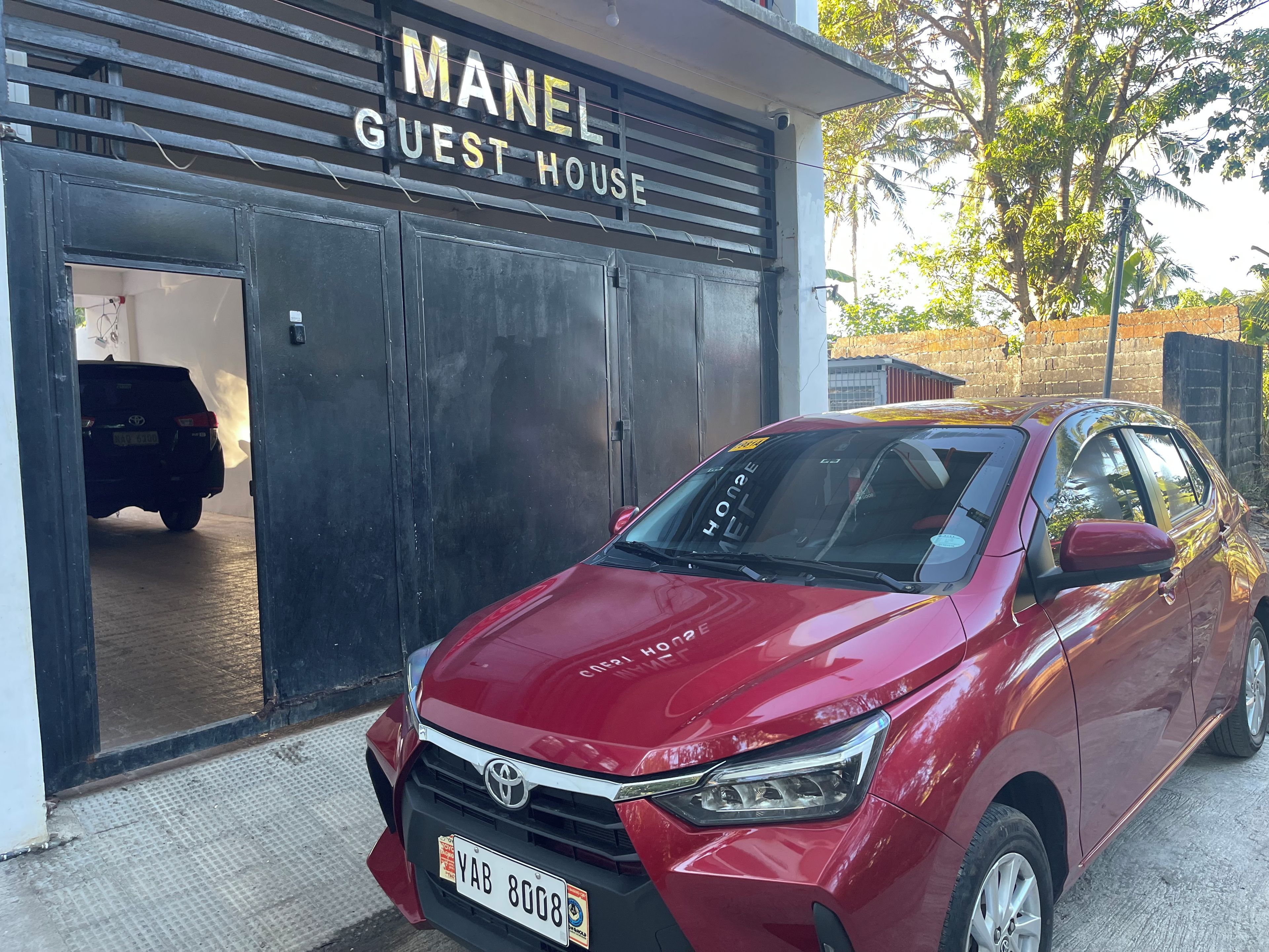 Une Toyota Corolla rouge était garée devant un bâtiment portant l’inscription « MANEL GUEST HOUSE ».
