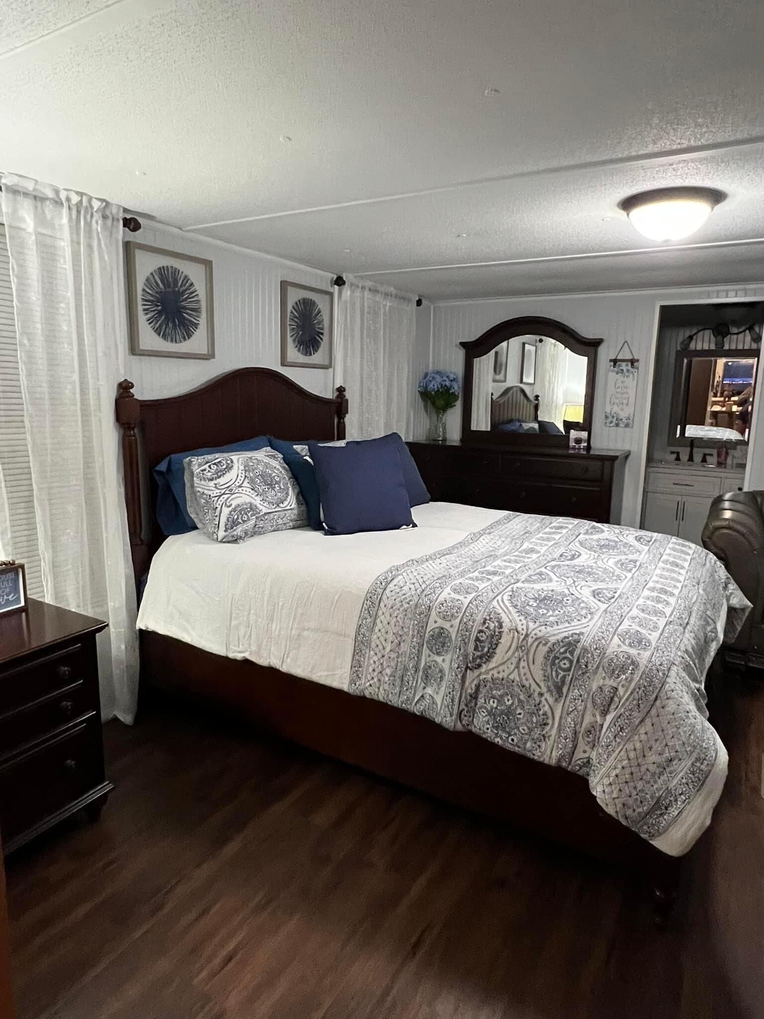 A neatly arranged bedroom with a wooden bed, a nightstand, a dresser, and a mirror.