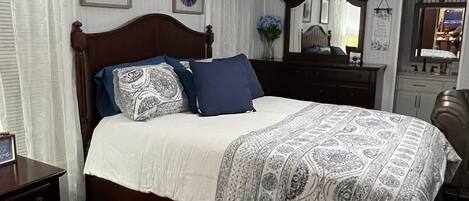 A neatly arranged bedroom with a wooden bed, a nightstand, a dresser, and a mirror.