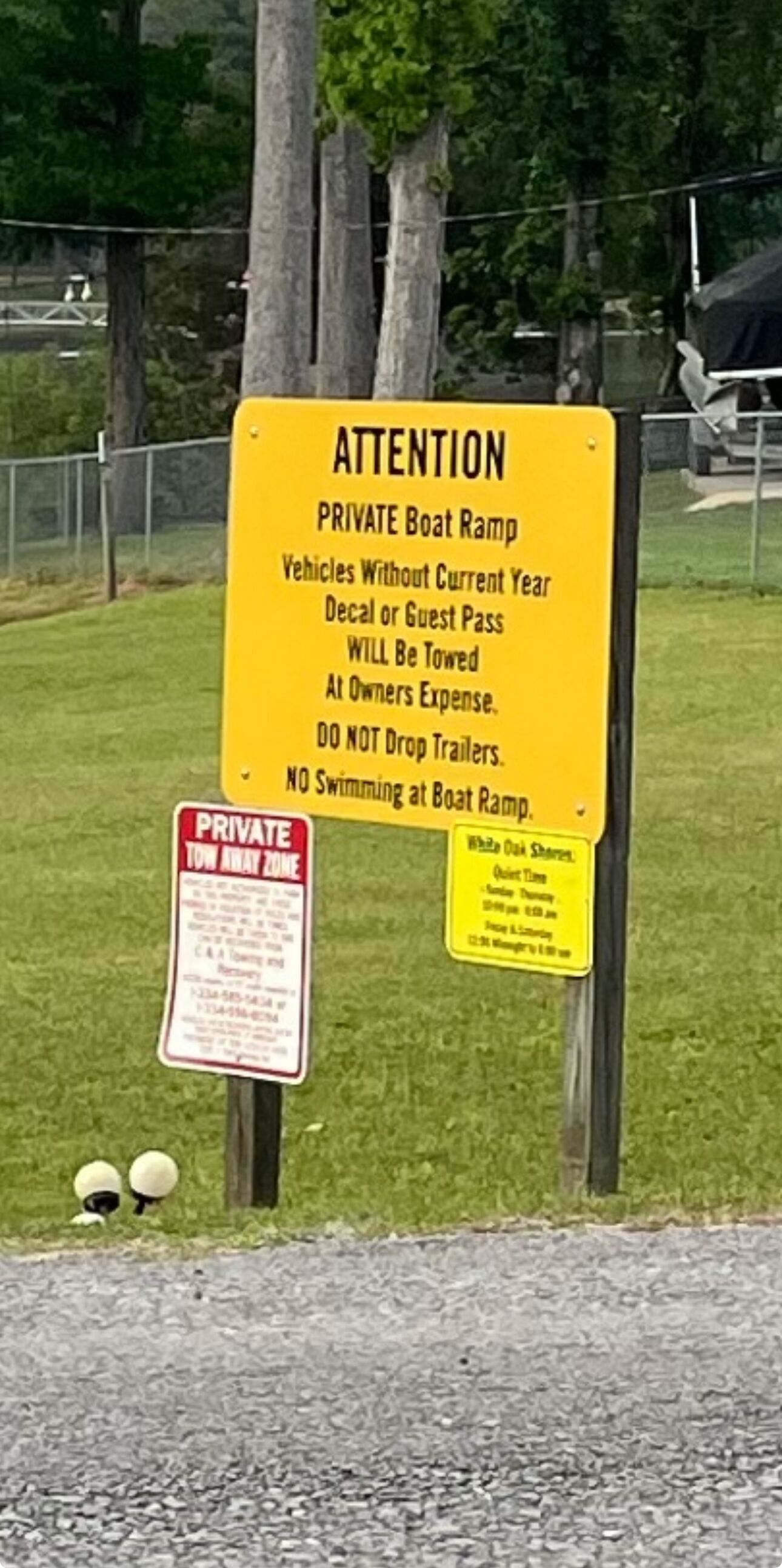 A yellow sign with text about a private boat ramp, towing warnings, and a no swimming notice.