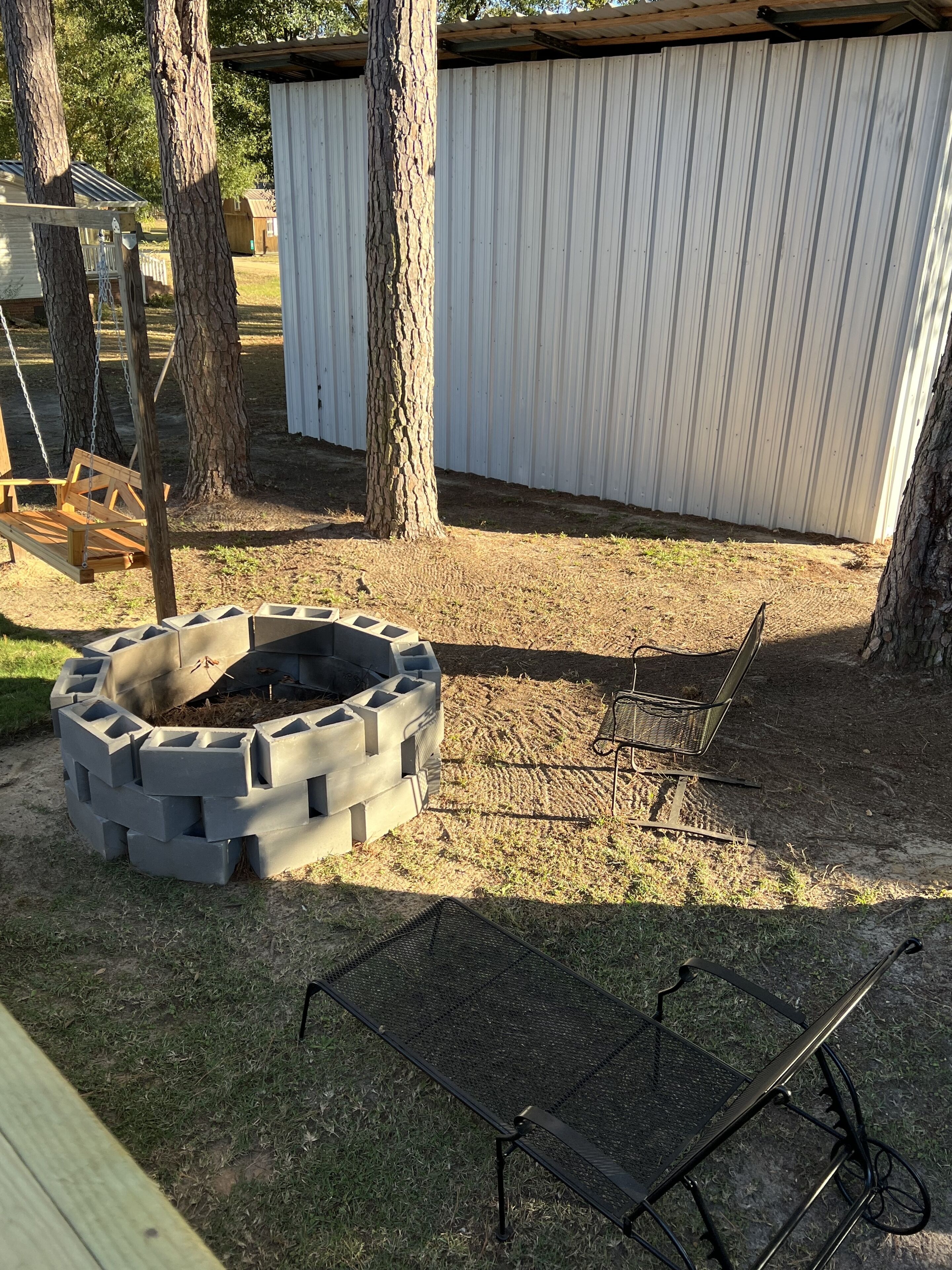 A backyard with a fire pit, a swing set, and a metal chair.