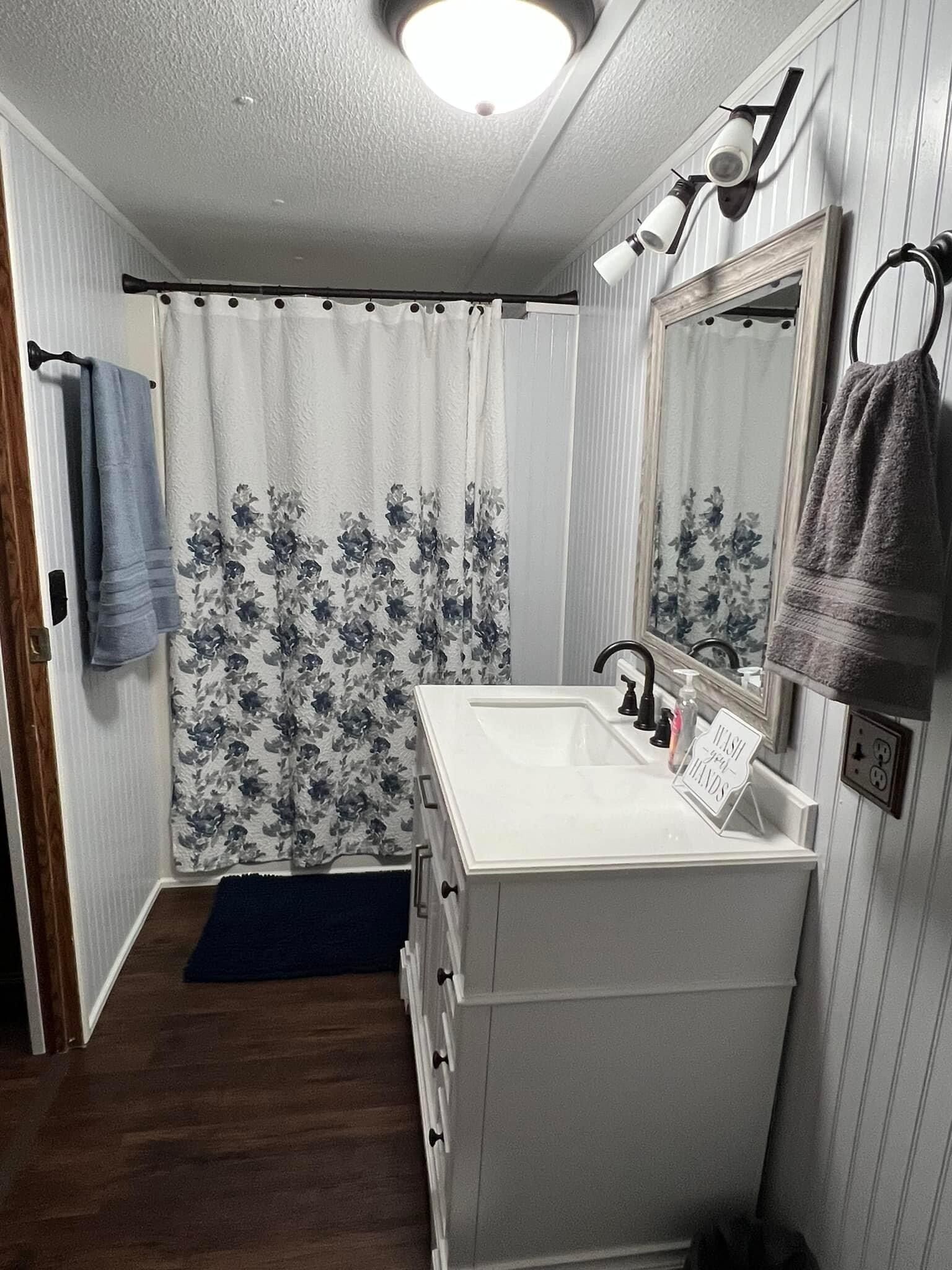 Casa de banho com uma pia branca, um espelho, uma cortina de chuveiro estampada com flores e um porta-toalhas.