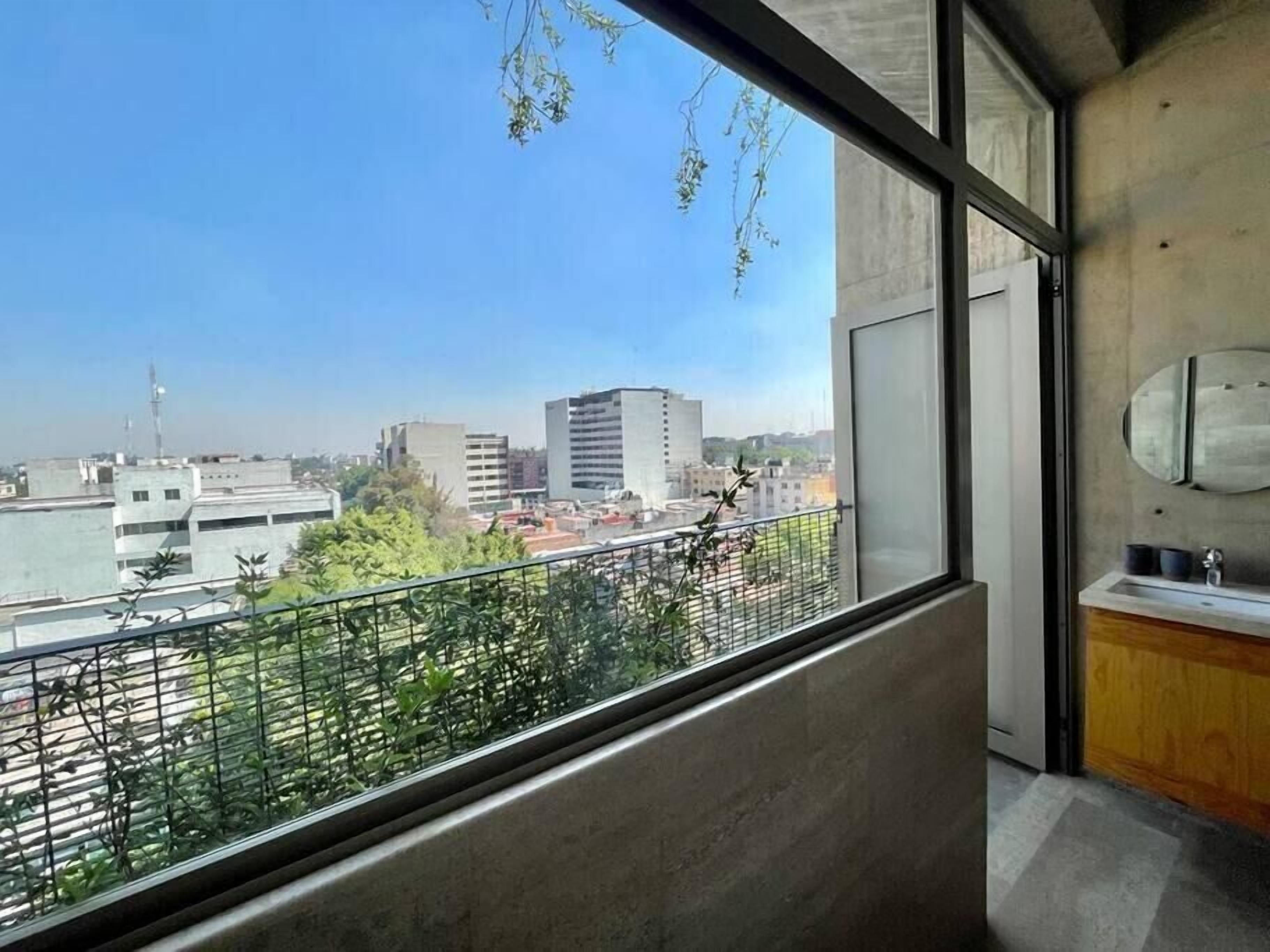 A modern bathroom with a large window, a concrete wall, and a view of the cityscape.
