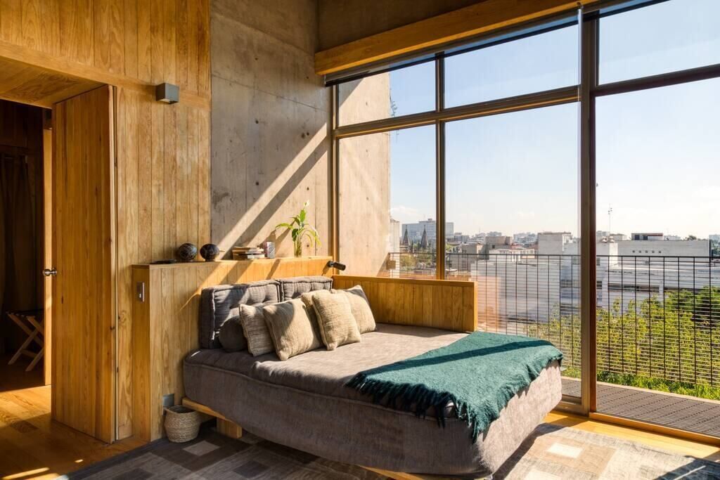 A modern bedroom with a large window, a wooden headboard, and a city view.