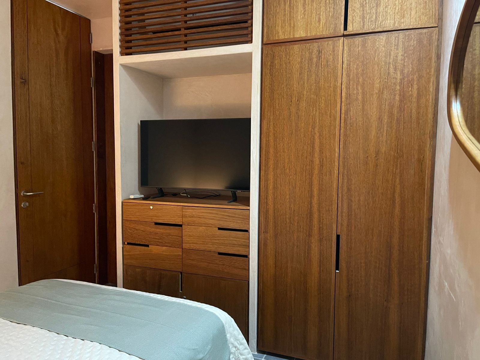 A bedroom with a bed, wooden wardrobe, and a television on a wooden cabinet.