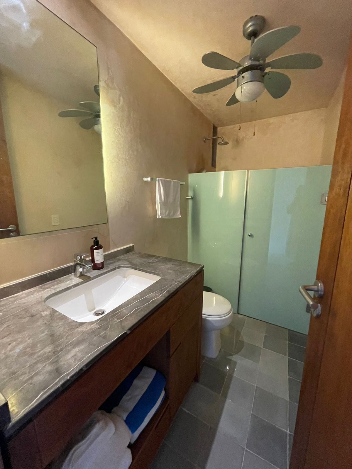 A bathroom with a double vanity, a ceiling fan, and a glass shower enclosure.