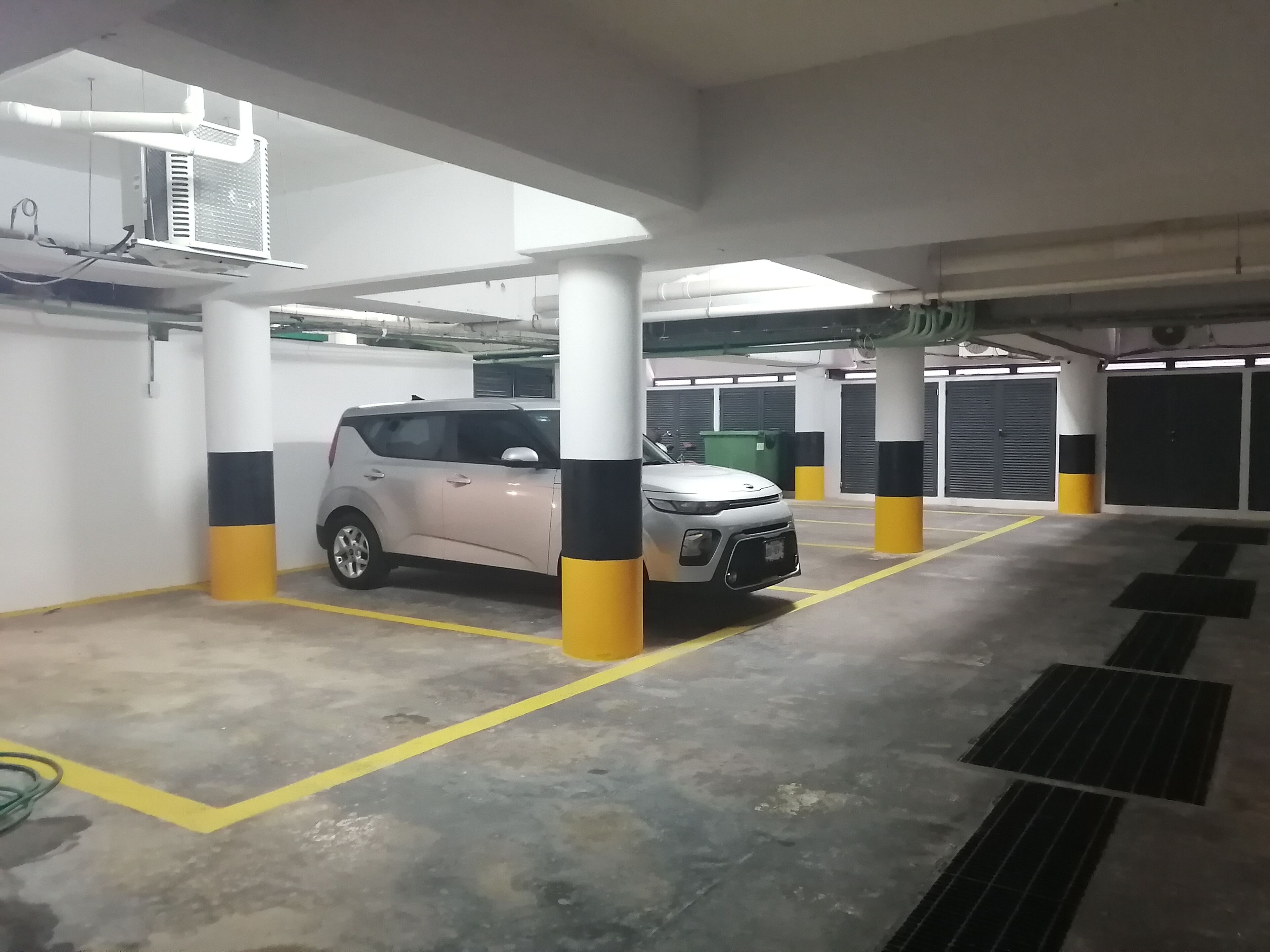A parking garage with white pillars, yellow and black stripes, and a silver car parked in a bay.