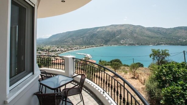 Een balkon met tafel en stoelen met uitzicht op een kustlandschap met bergen en een wateroppervlak.