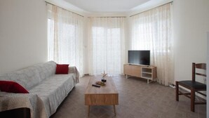 Een woonkamer met een bank, een houten salontafel, een tv op een meubel en een fauteuil.