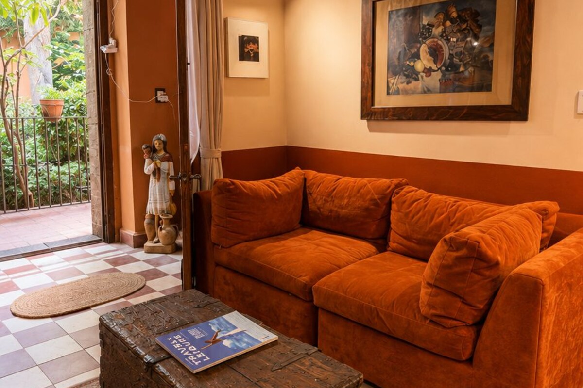 Une pièce avec un sol à carreaux, un banc en bois sur lequel repose un livre, un canapé orange et un tableau accroché au mur.
