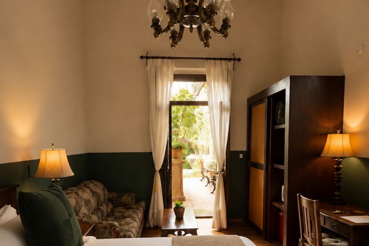 Une chambre d’hôtel avec un grand lit, un lustre, un bureau avec une chaise et une vue sur l’extérieur par une fenêtre.
