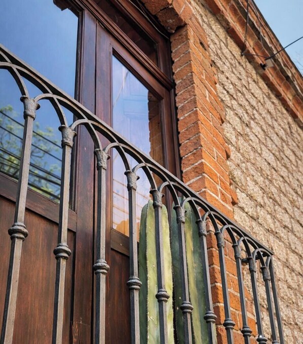 A balcony with wrought iron railings and a wooden door, set against a brick wall. - Hacienda Gobernadores – Boutique Stay in a Historic 19th-Century Hacienda (Mexico City)