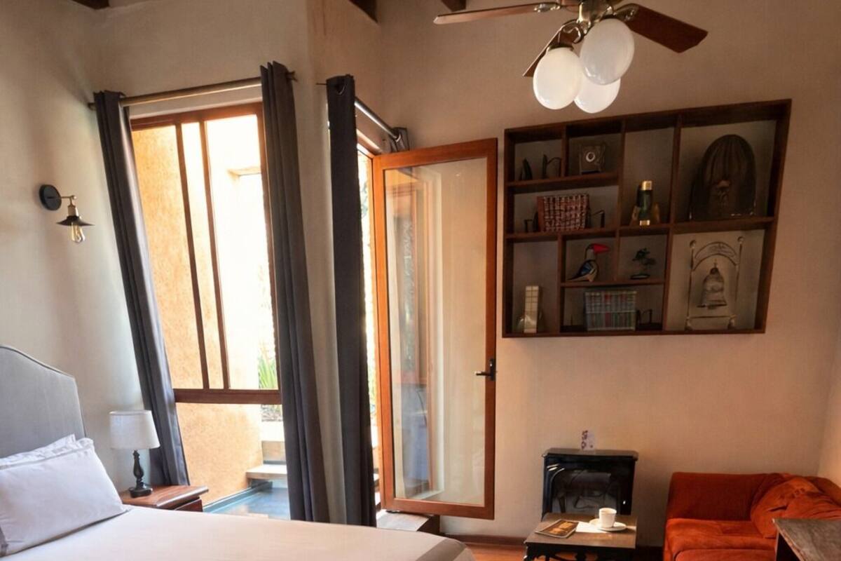 Un dormitorio con una cama grande, un ventilador de techo de madera, una mesita, un sofá rojo y una estantería.