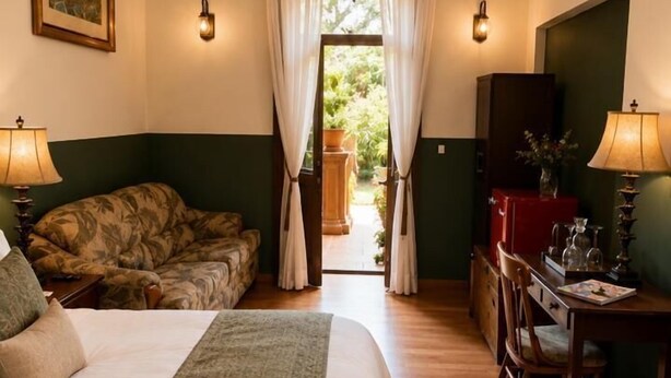 Un dormitorio con cama, escritorio, silla, candelabro y vistas al exterior.