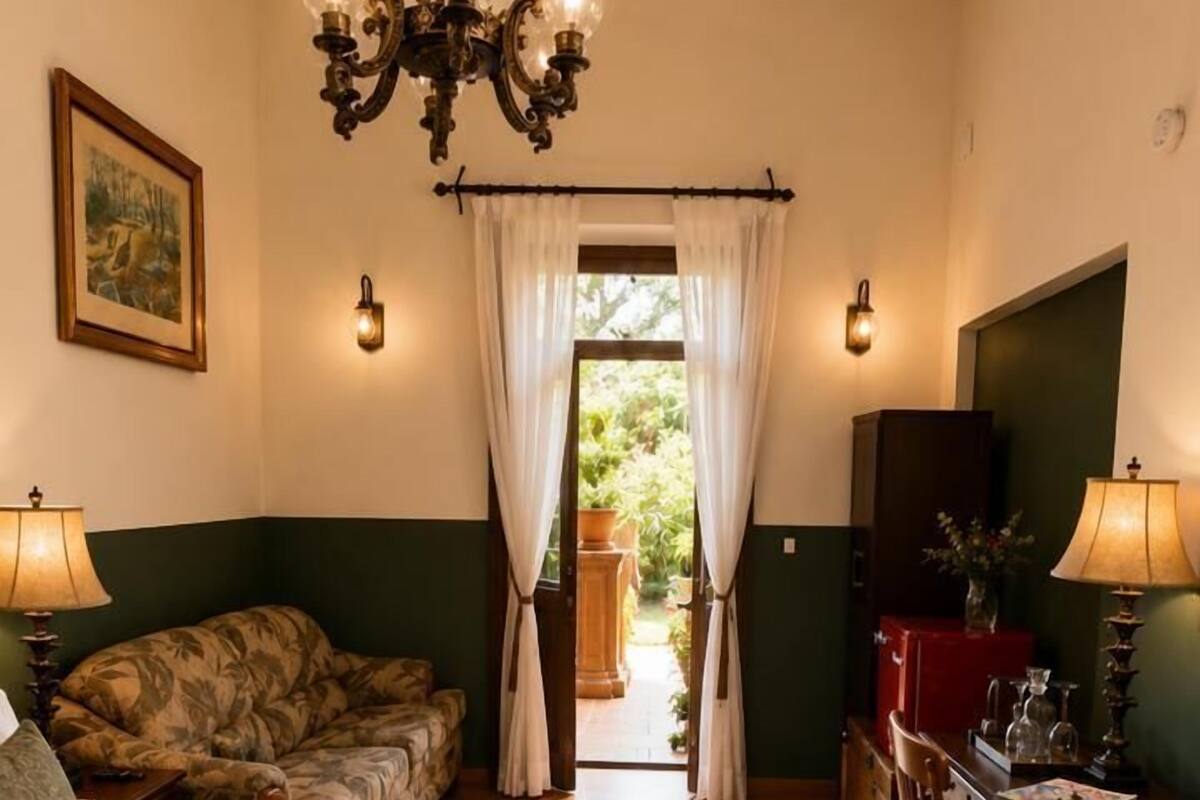 Un dormitorio con cama, escritorio, silla, candelabro y vistas al exterior.