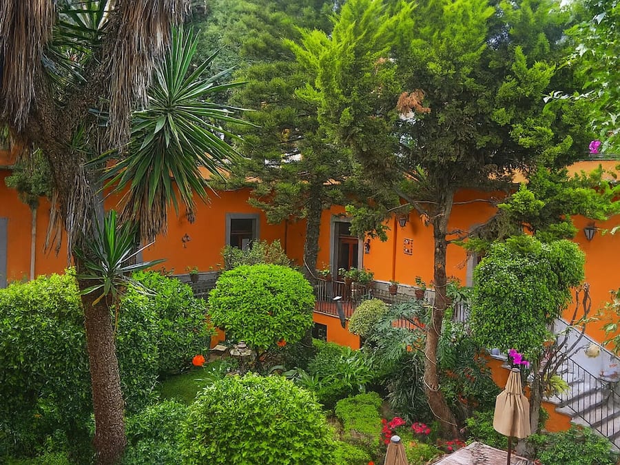 An orange building with a courtyard surrounded by lush greenery and a palm tree.