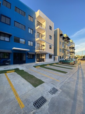 Un immeuble d’appartements moderne doté de nombreux balcons, d’un espace de stationnement et d’une pelouse bien entretenue.