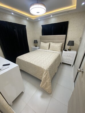 Une chambre à coucher comprenant un lit, deux tables de chevet, un bureau et un luminaire moderne au plafond.