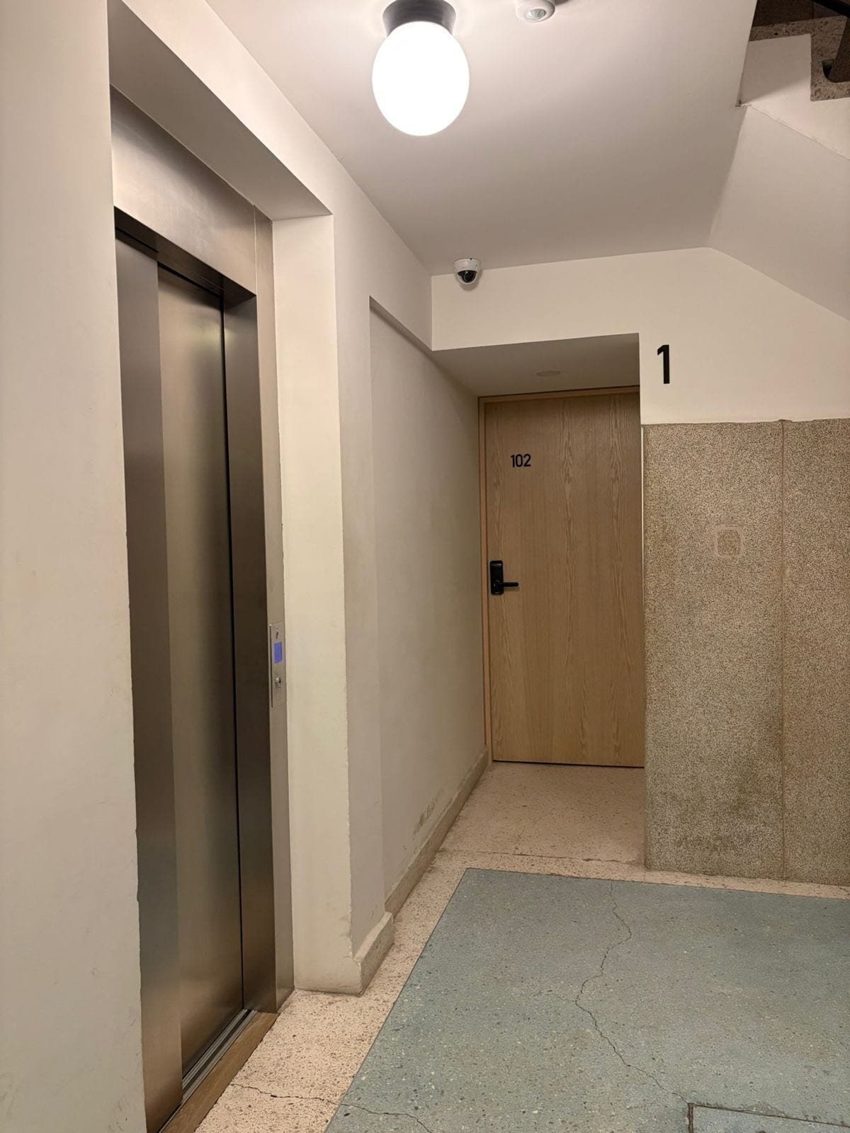 Un couloir avec un ascenseur, une porte portant l’inscription « 102 », et le chiffre « 1 » peint sur le mur.