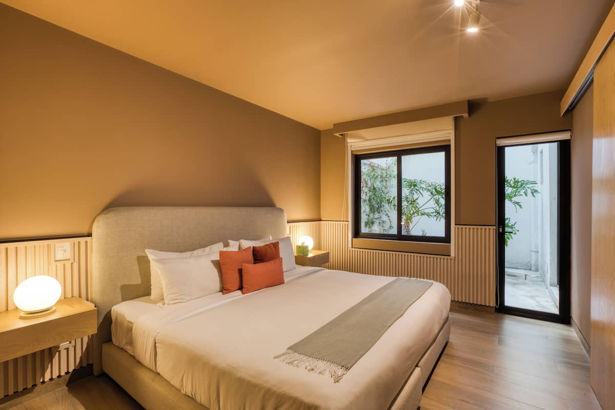 Ein modernes Schlafzimmer mit einem großen Bett, Nachttischlampen und Blick ins Freie durch ein Fenster.