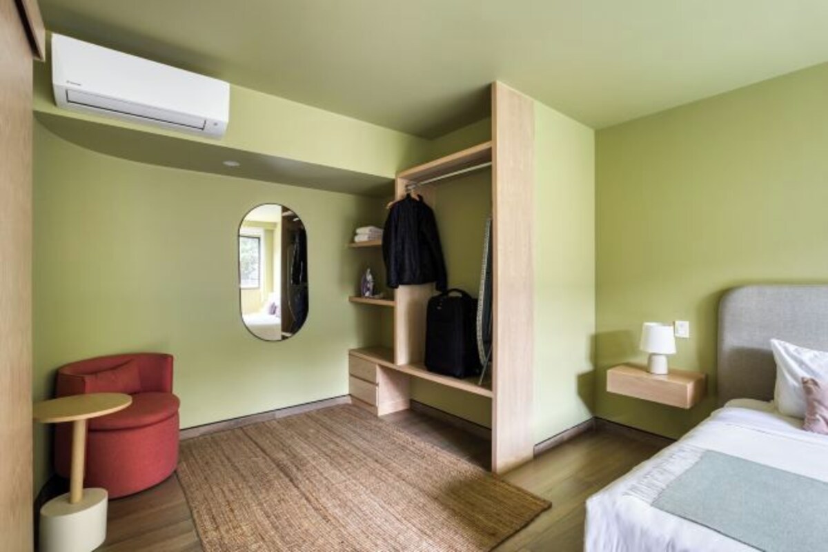Una habitación de hotel con una cama, un sillón rojo, una mesita, un armario y un espejo.
