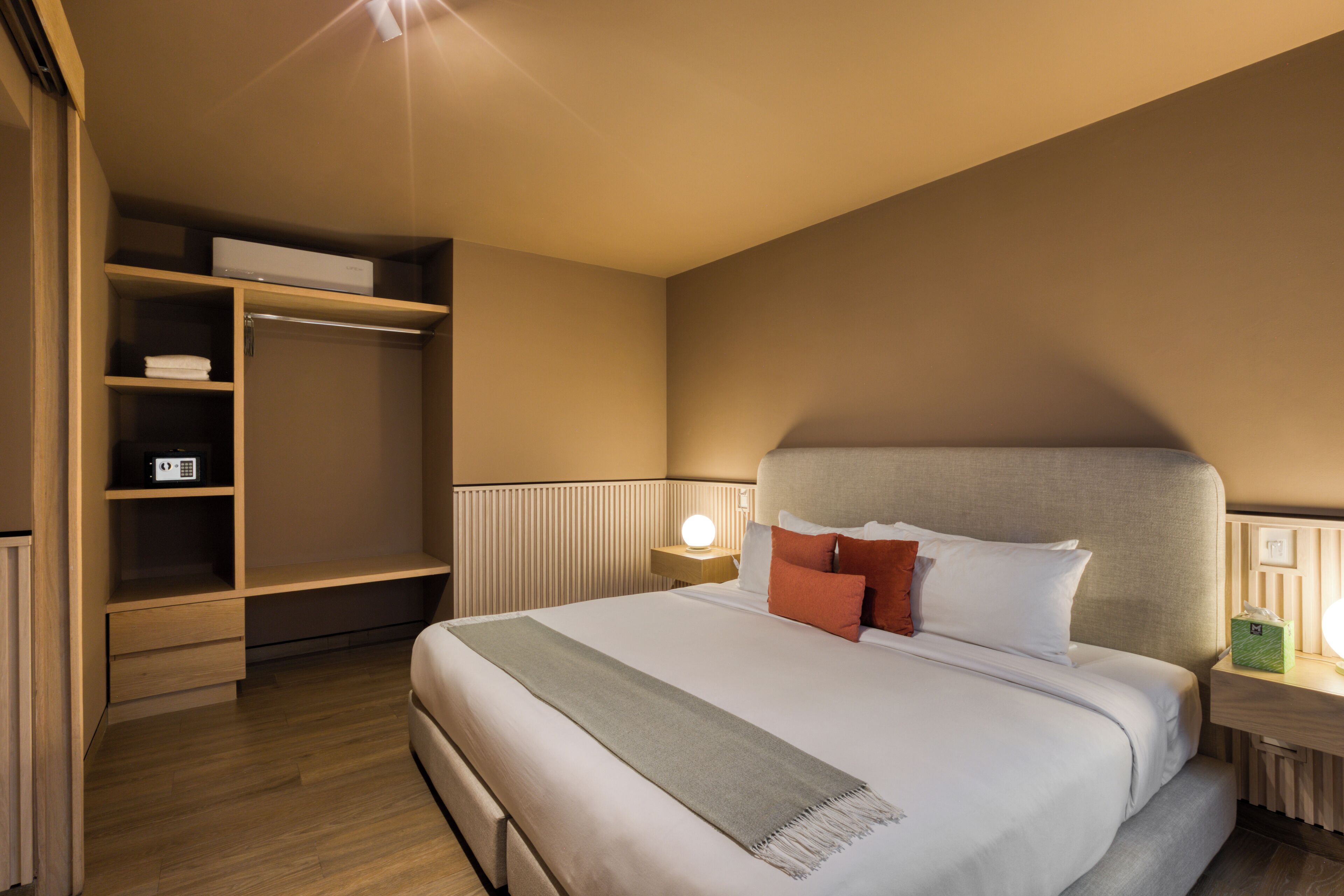 A hotel room with a large bed, a bedside table with a lamp, a wardrobe, and a shelf with a radio.