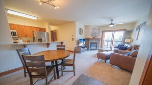 A modern kitchen with wooden cabinets, a dining table, and chairs. There is a living area with a sofa and a fireplace. - Oro Grande 308 (Keystone)