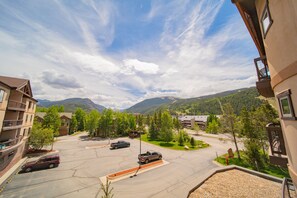 A parking lot with several cars, surrounded by buildings and trees, with mountains in the background. - Oro Grande 308 (Keystone)