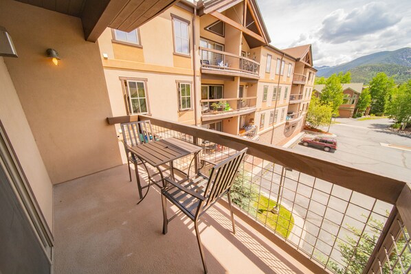 A balcony with a table and chairs, overlooking a parking area and a mountain view.
