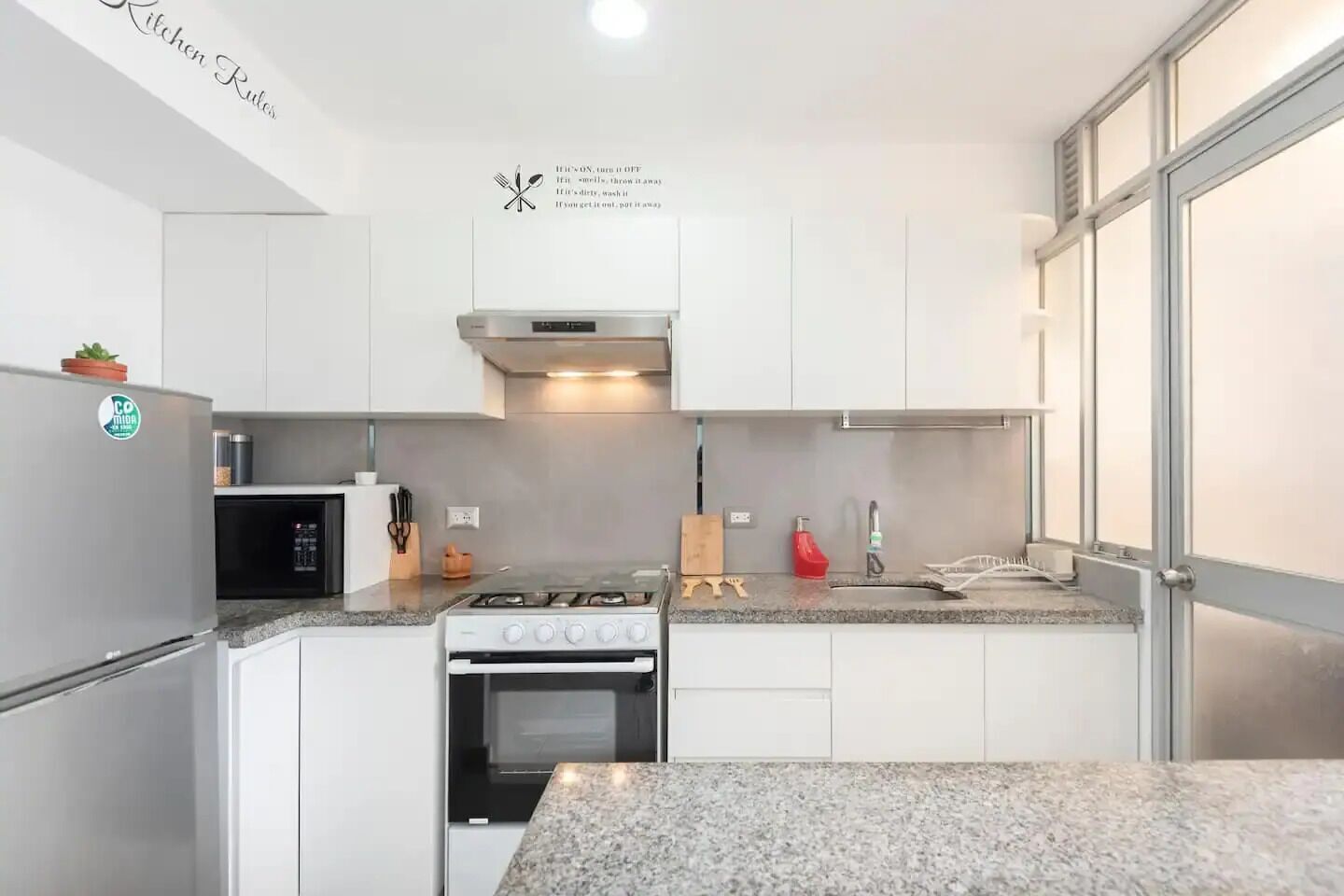 Una cocina moderna con armarios blancos, una estufa de acero inoxidable, un microondas y una cocina a gas.
