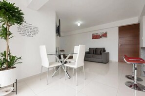 Un salon moderne avec une table à manger en verre, des chaises blanches, un canapé gris et un banc rouge.