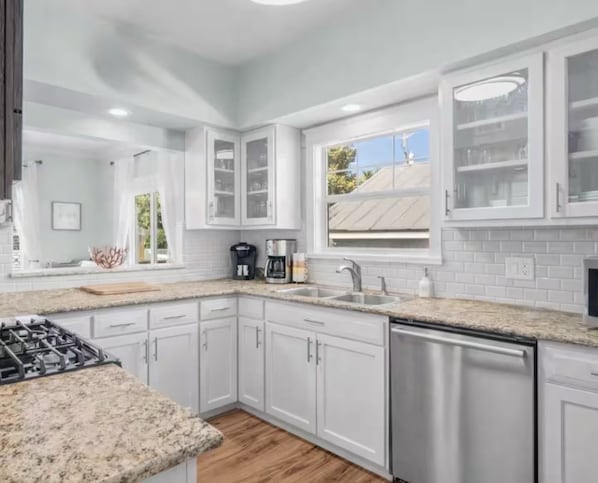 A modern kitchen with white cabinetry, a granite countertop, and a dishwasher.