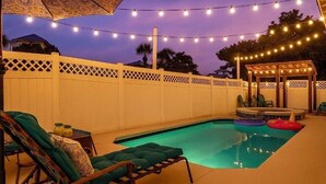 Ein Garten mit Schwimmbad, Liegestühlen und Lichterketten.
