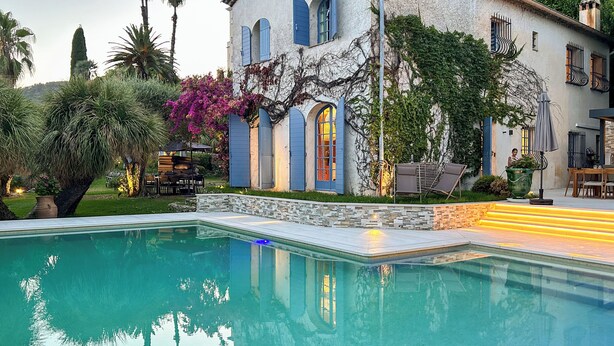A swimming pool with a stone border, a patio area with outdoor furniture, and a building with blue shutters and a garden. - Historic Villa 9 people, Private Pool, near Cannes (Grasse)