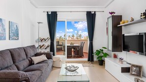 Un salon moderne avec un canapé gris, une table basse en verre, un téléviseur et un balcon comprenant un coin repas.