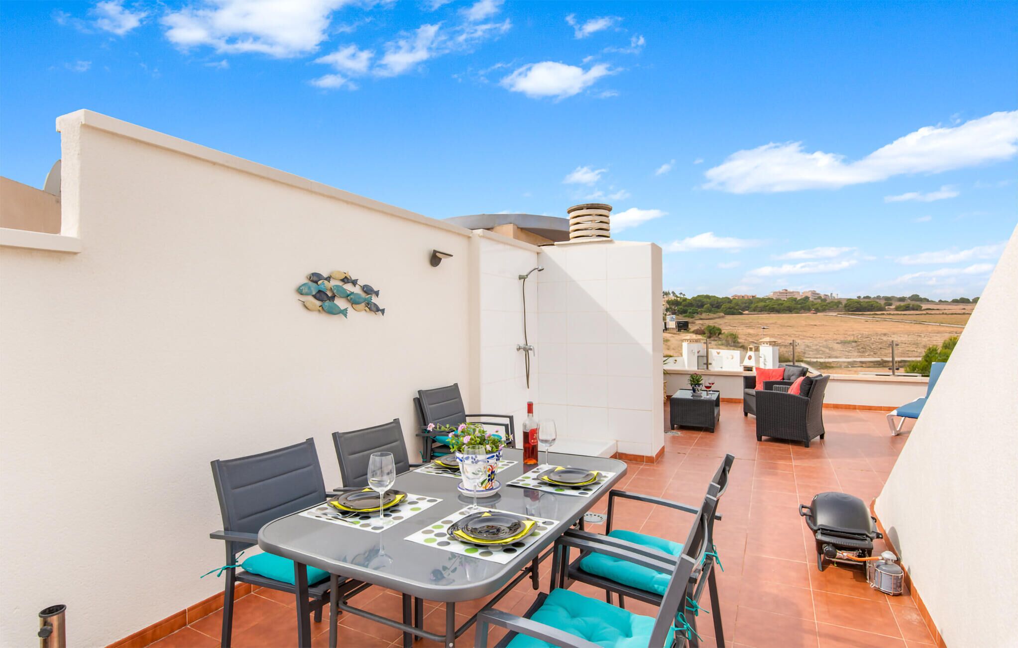 A rooftop terrace with a dining table set for four, outdoor seating, and a view of the landscape.