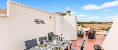 A rooftop terrace with a dining table set for four, outdoor seating, and a view of the landscape.
