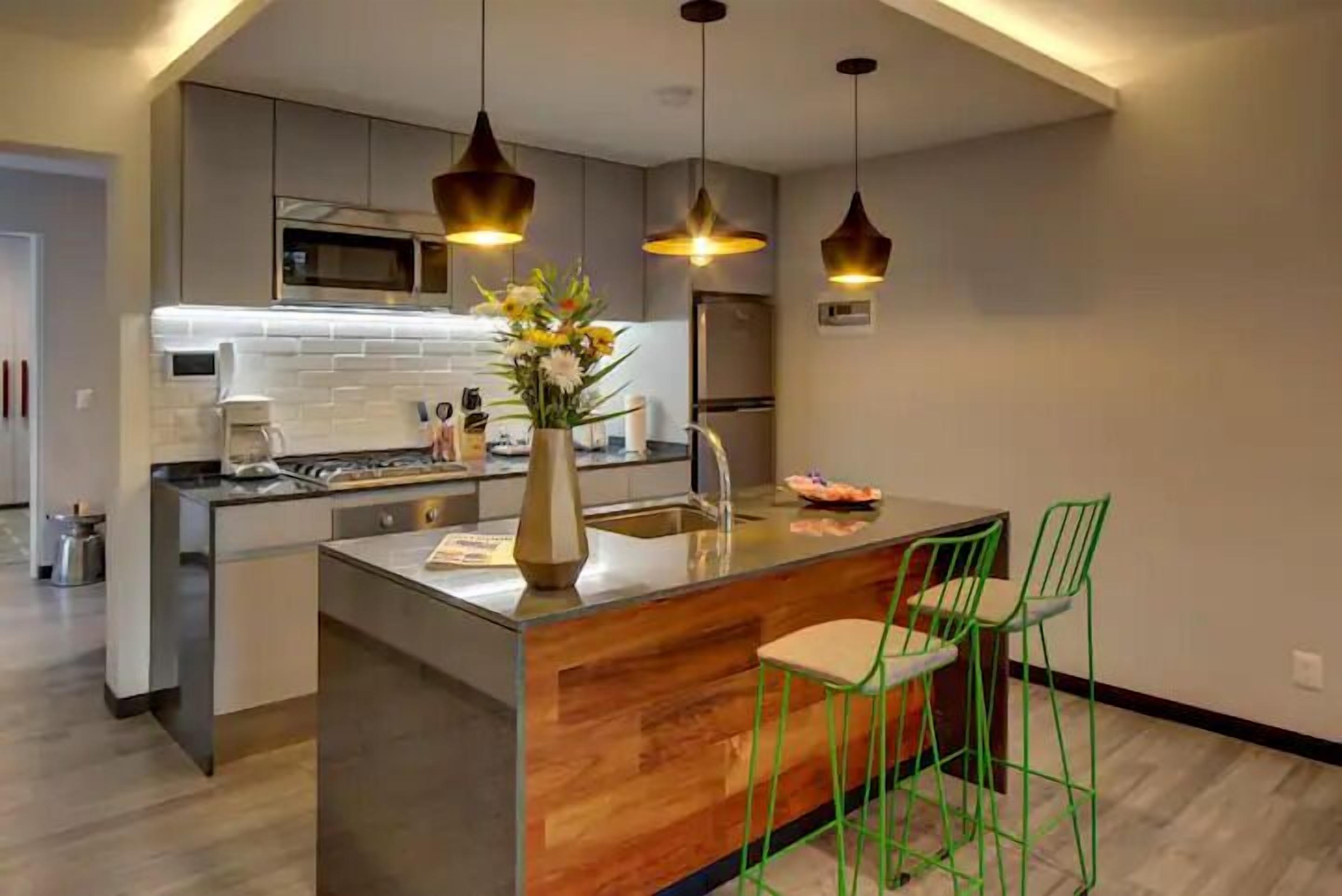 Una cocina moderna con una isla central, electrodomésticos de acero inoxidable y taburetes de bar verdes.