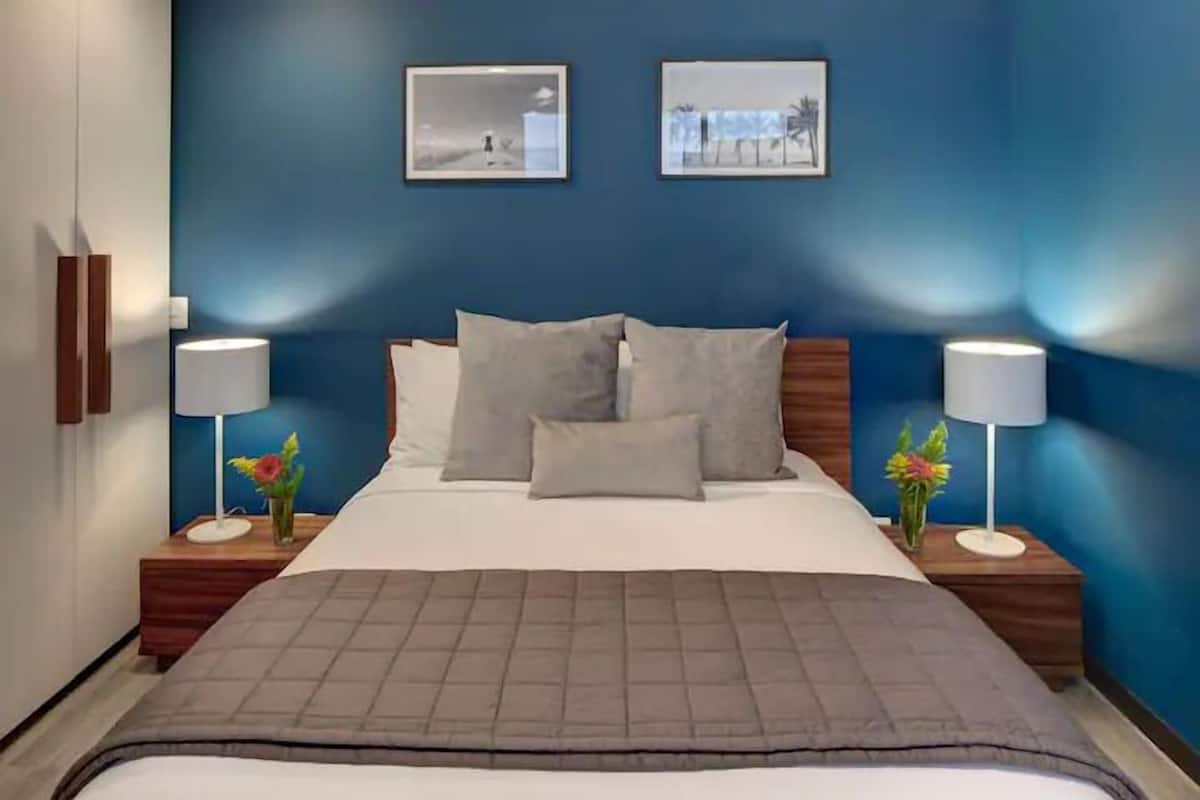Une chambre d’hôtel avec un grand lit, deux tables de chevet avec des lampes et deux tableaux encadrés au mur.
