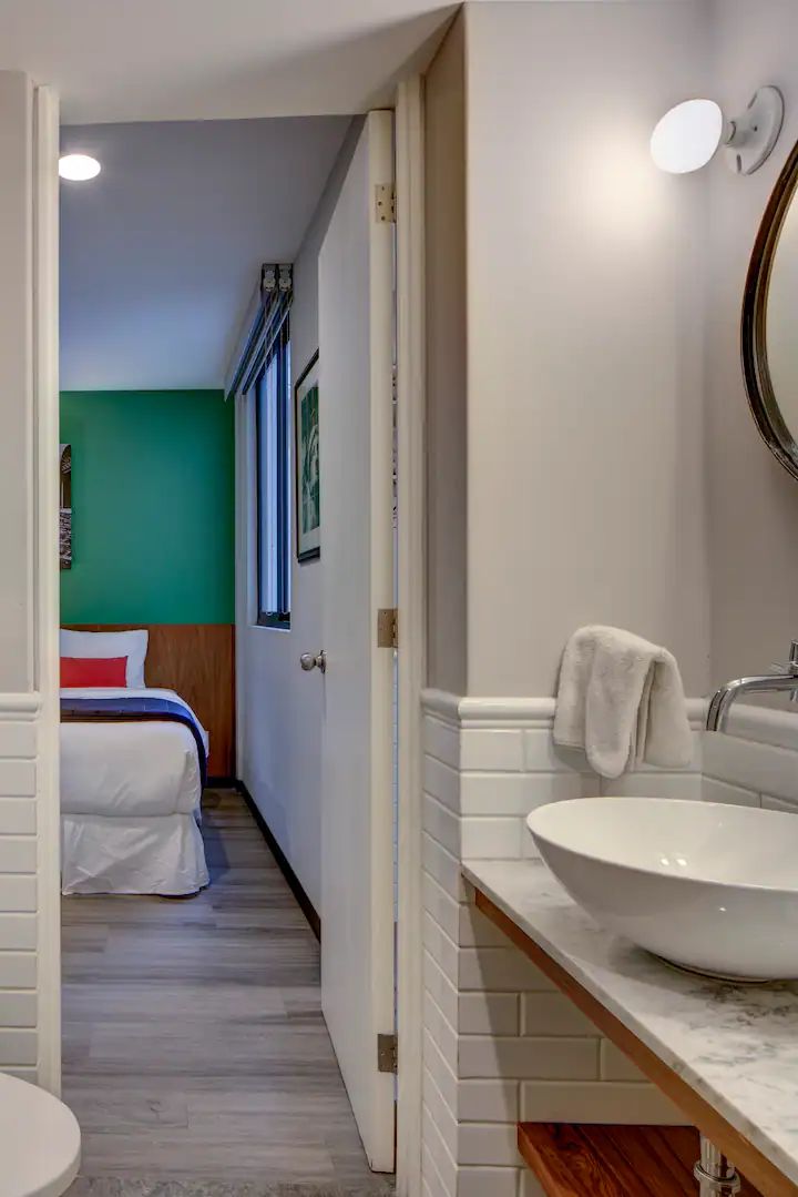 A hotel room with a bed, a white sink, and a mirror.