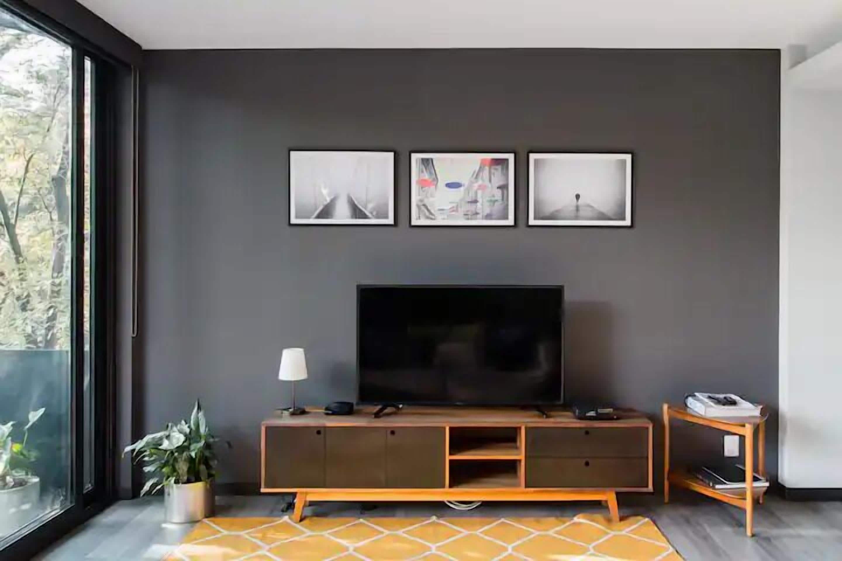 A modern living room with a large flat-screen TV, a wooden entertainment unit, and three framed artworks on the wall.