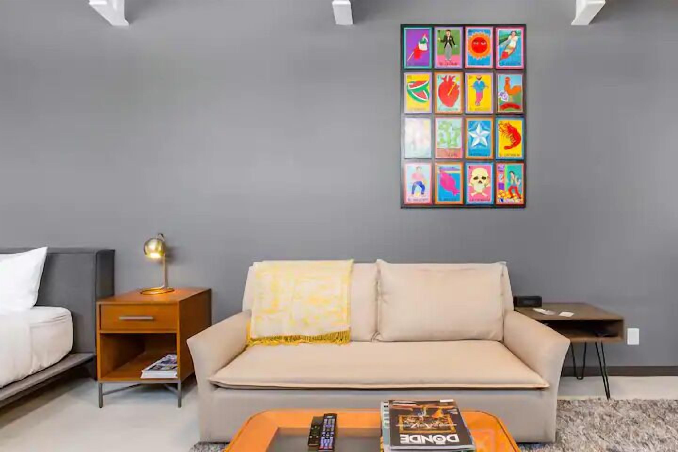 A modern living room with a grey sofa, a small wooden side table with a lamp, and a coffee table with a remote control and a book.