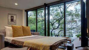 Un dormitorio moderno con una cama grande, un escritorio y vistas a árboles a través de amplias ventanas.