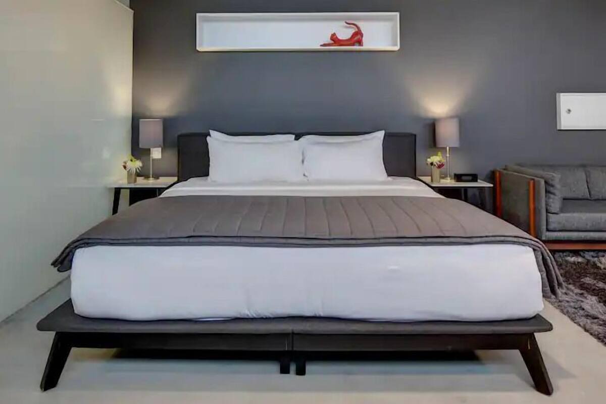 Une chambre à coucher moderne avec un grand lit, des tables de chevet avec des lampes, un canapé gris et une sculpture rouge accrochée au mur.