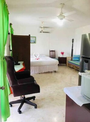 A hotel room with a bed, a desk with a computer, a chair, a ceiling fan, and a TV. - Peaceful Ocean View Studio  (Puerto Plata)