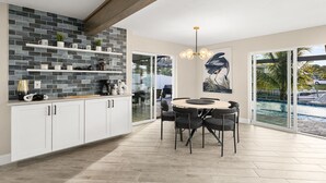 A modern kitchen with white cabinets, a stone backsplash, and a dining area with a round table and chairs. - Waterfront Bliss w/ Dock - Sunsets Over Del Prado (Cape Coral)