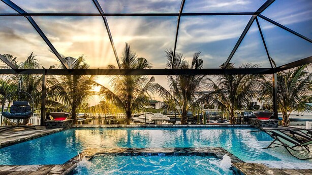 A pool area with a hot tub, lounge chairs, and palm trees. - Waterfront Bliss w/ Dock - Sunsets Over Del Prado (Cape Coral)